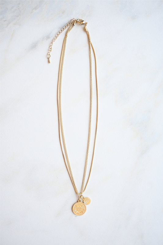 The layered gold coin necklace is laying on a white marble tile.