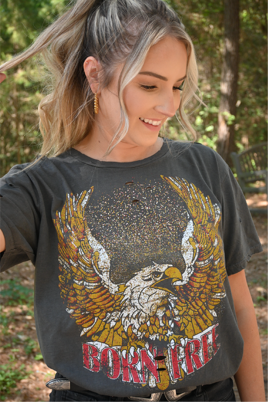 A close up shot of a woman looking down smiling wearing the born free graphic tee.