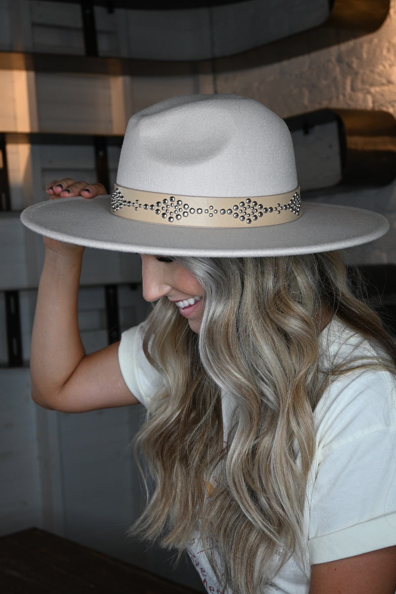 A side view of a blonde woman holding her ivory faux leather band fedora hat.