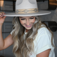 A woman is smiling and holding her ivory faux leather band fedora hat.