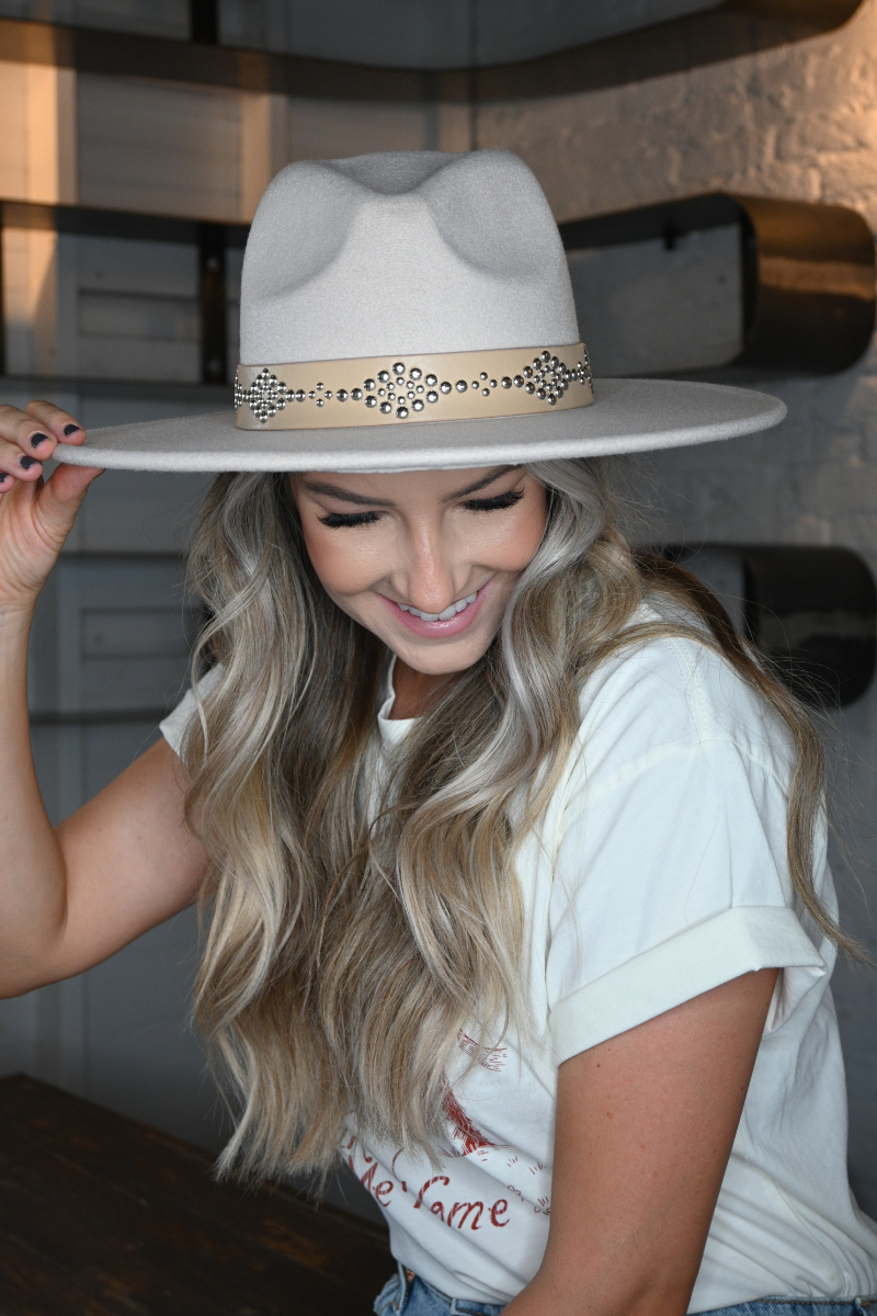 A woman is smiling and holding her ivory faux leather band fedora hat.