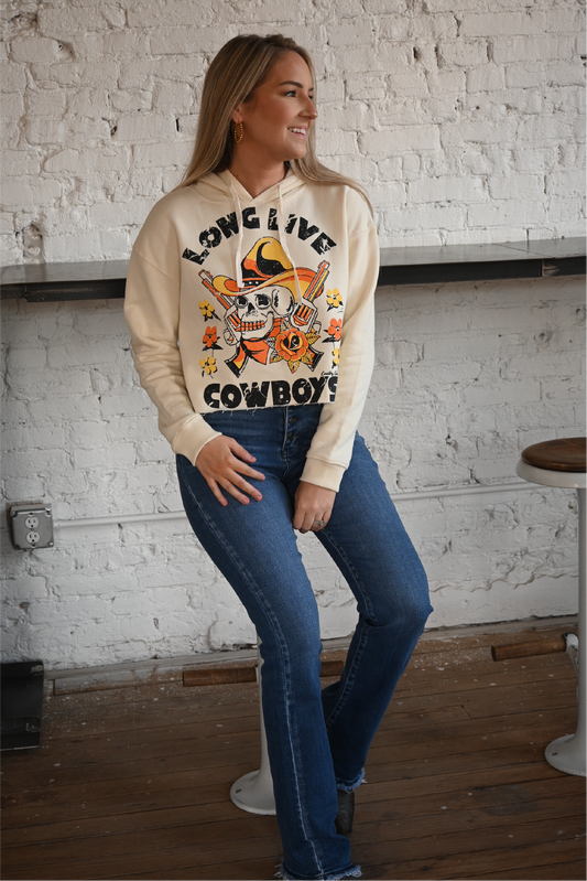 A woman is sitting on a stool wearing long live cowboys hoodie paired with the high rise bootcut kancan jeans.