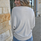 A close up of the back of an oatmeal crew neck sweater on a woman.