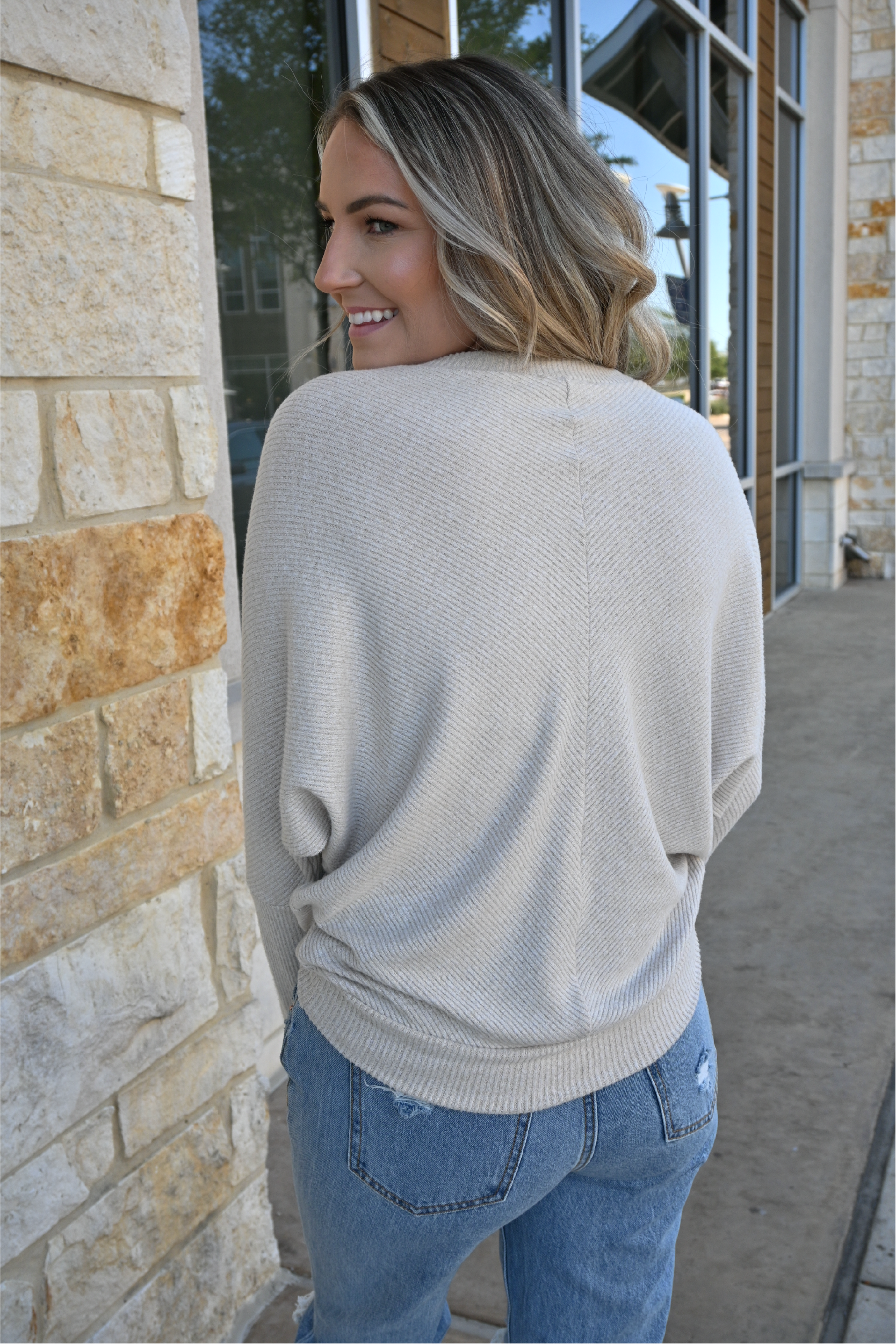 A close up of the back of an oatmeal crew neck sweater on a woman.