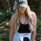 A woman is looking down wearing a olive corduroy mama hat with a black ribbed cropped cami  and dark grey distressed skinny jeans with a distressed denim jacket around her waist.