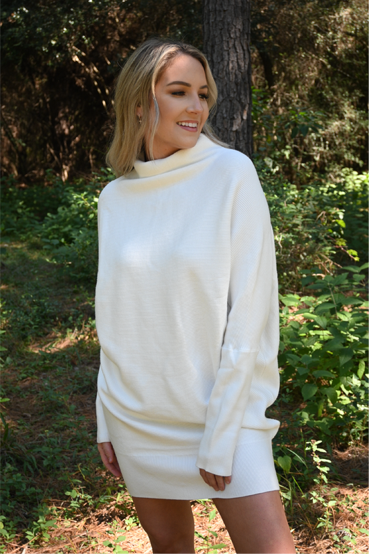 A woman is facing the camera looking off smiling wearing the slouch neck sweater dress.