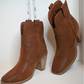 A close up shot of both sides of the western cognac booties on a white bench.