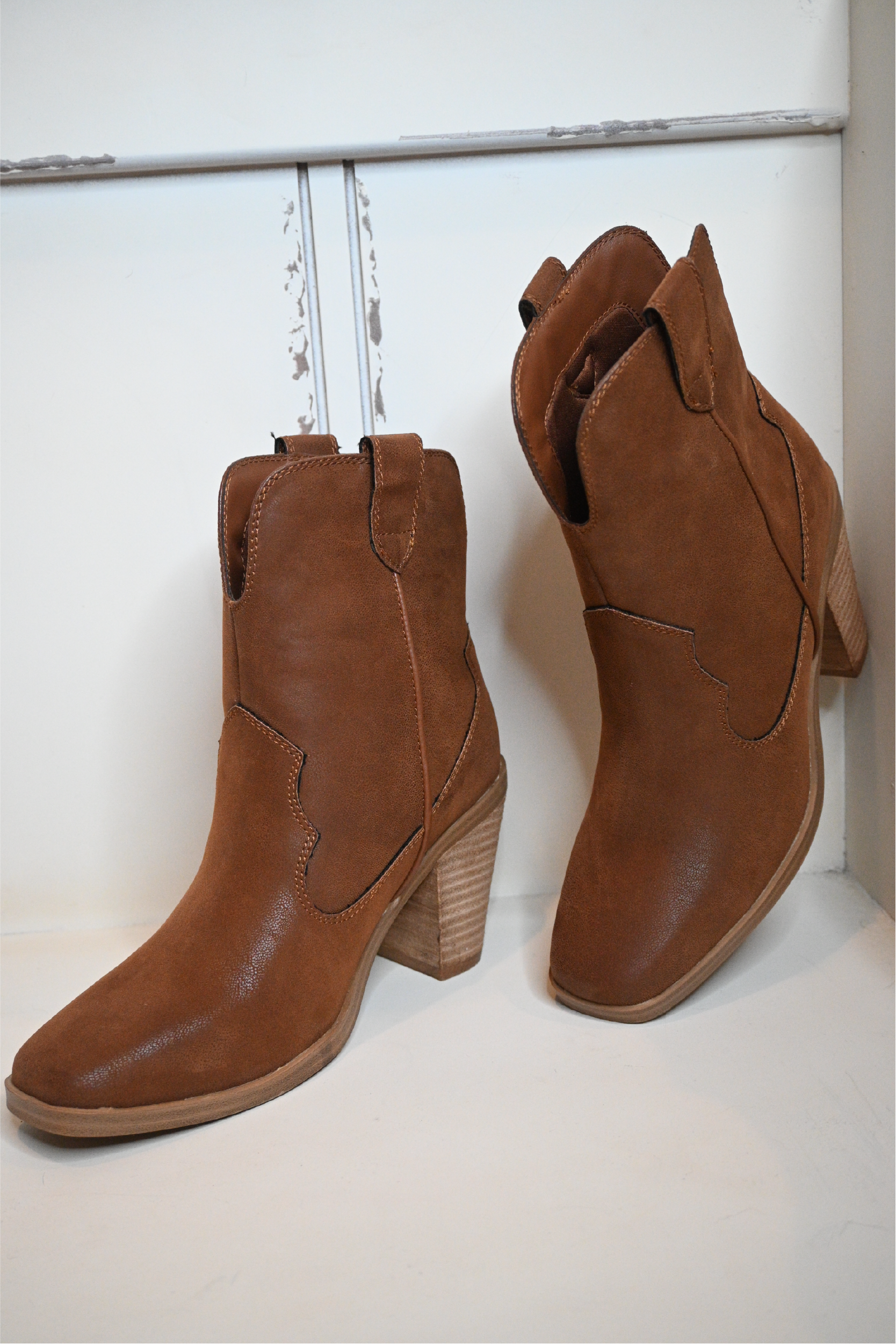 A close up shot of both sides of the western cognac booties on a white bench.