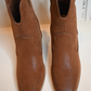A close up shot of the front of the western cognac booties on a white bench.