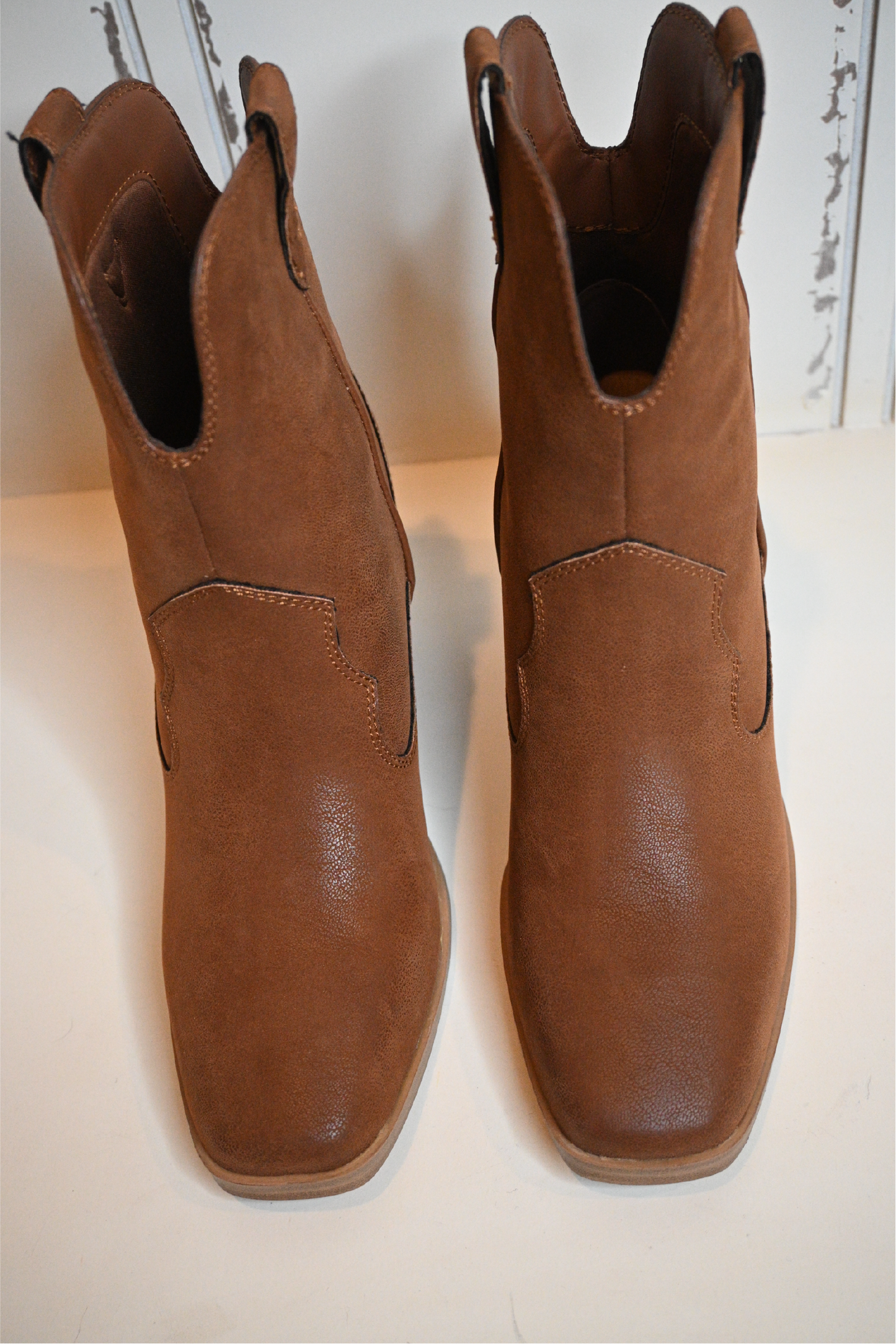 A close up shot of the front of the western cognac booties on a white bench.