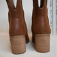 A close up of the back of the western cognac booties on a white bench.