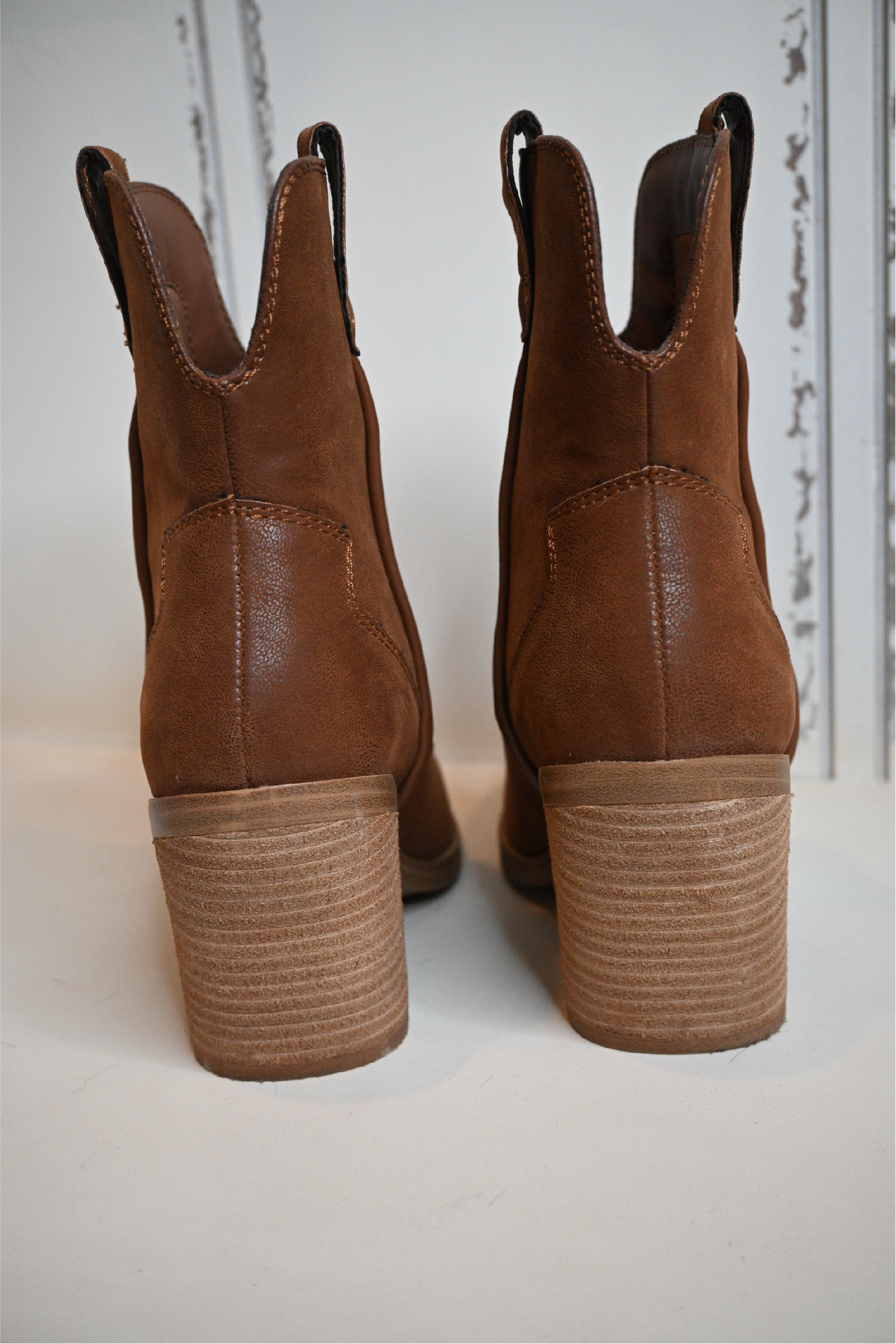 A close up of the back of the western cognac booties on a white bench.