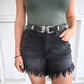 A woman is wearing a hunter green bodysuit and black frayed high rise shorts paired with a black leather belt.