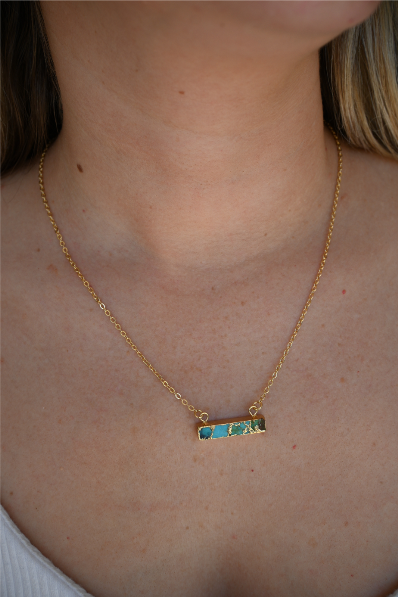 A close up image of a women wearing the turquoise bar gold necklace.