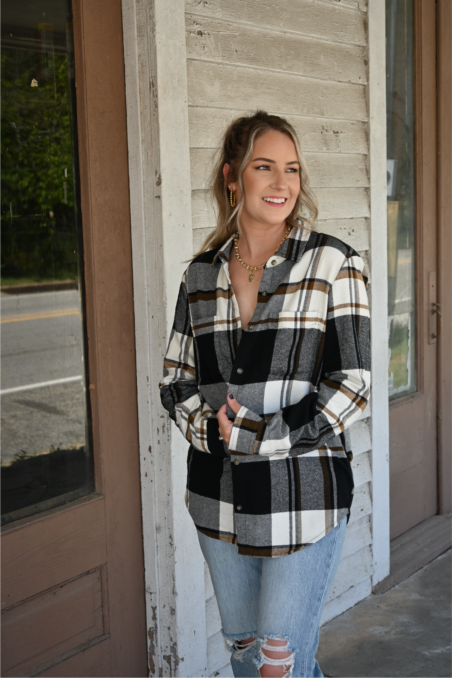 Model is smiling looking away from the camera holding the black brown plaid button down together paired with the 90's skinny high rise jeans and the gold chain neckalce and gold coin necklace.