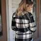 Model has her back to the camera looking down to the side wearing the black brown plaid button down paired with the 90's skinny high rise jeans.
