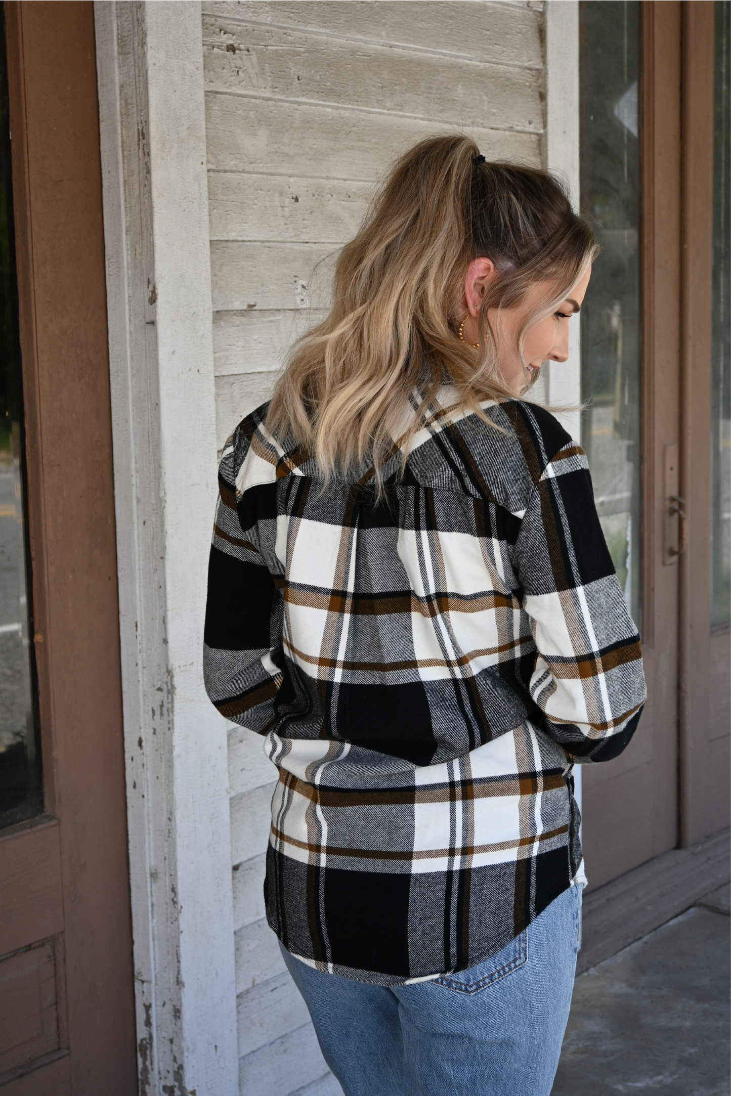 Model has her back to the camera looking down to the side wearing the black brown plaid button down paired with the 90's skinny high rise jeans.