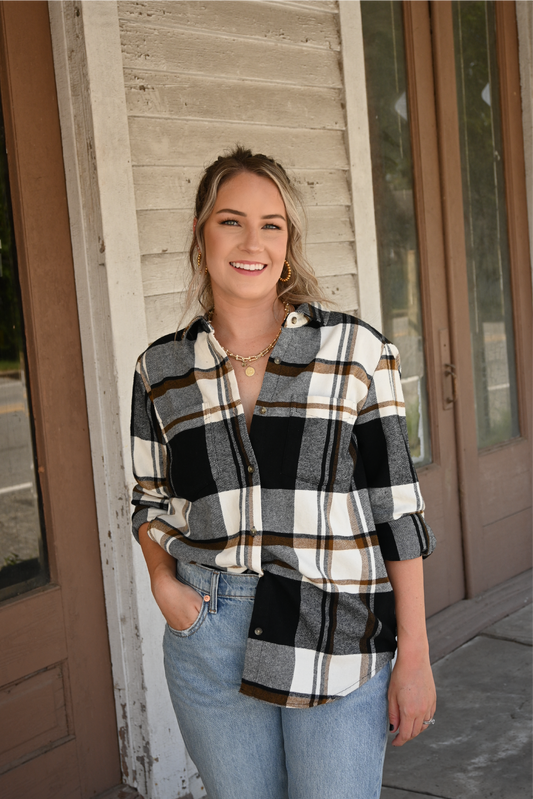 Model is smiling looking at the camera with one hand in her pocket and the other hand by her side. She is wearing the black brown plaid button down with one side tucked in the 90's skinny high rise jeans. She is also wearing the gold chain necklace paired with the gold coin necklace.