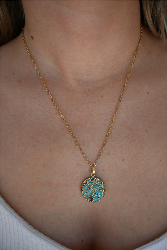 A close up image of a women wearing a circle turquoise stone gold necklace.