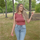 A women is looking off holding a piece of her hair. The other arm is by her side. She is wearing the dusty rose ribbed bodysuit paired with the 90's skinny high rise sneak peek jeans and triple gold necklace.