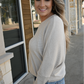 A woman is smiling looking away from camera wearing the oatmeal crew neck sweater tucked into the 90's high rise jeans