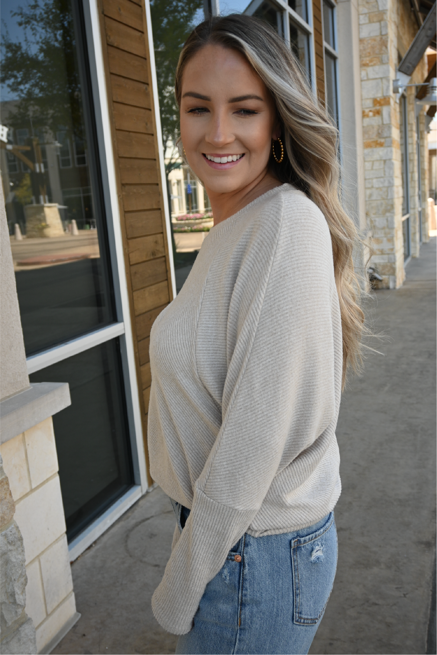 A woman is smiling looking away from camera wearing the oatmeal crew neck sweater tucked into the 90's high rise jeans