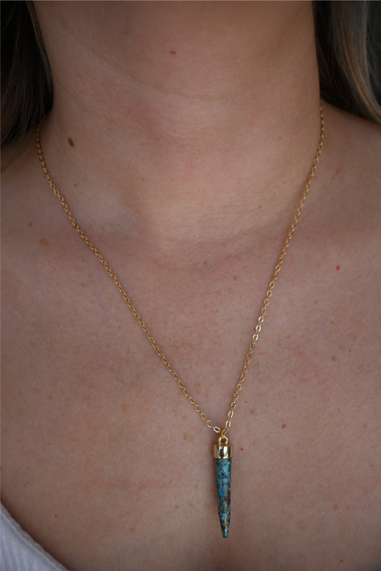 A close up image of a women wearing the turquoise spike gold necklace.