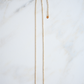 The turquoise bar gold necklace is laying on a white marble tile.