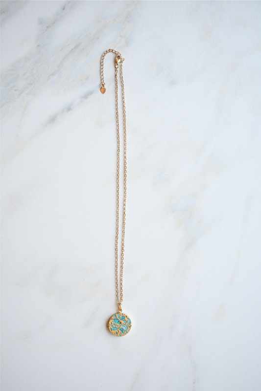 The circle turquoise stone necklace is laying on a white marble tile.