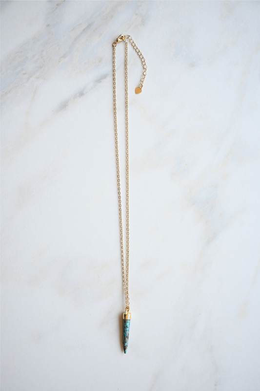 The turquoise spike gold necklace is laying on a white marble tile.